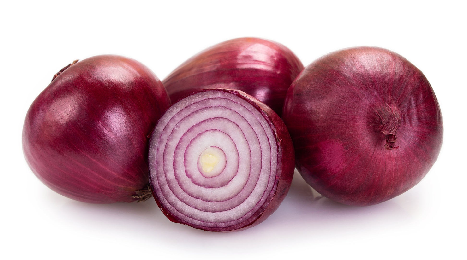 On display are 4 red onions, of the variety Short Red Creole. The red onions display their characteristic dark red shades. The onions are resting on a pure white surface. The red onion closest to us is cut in half, displaying the concentric rings of alternating red and white. 