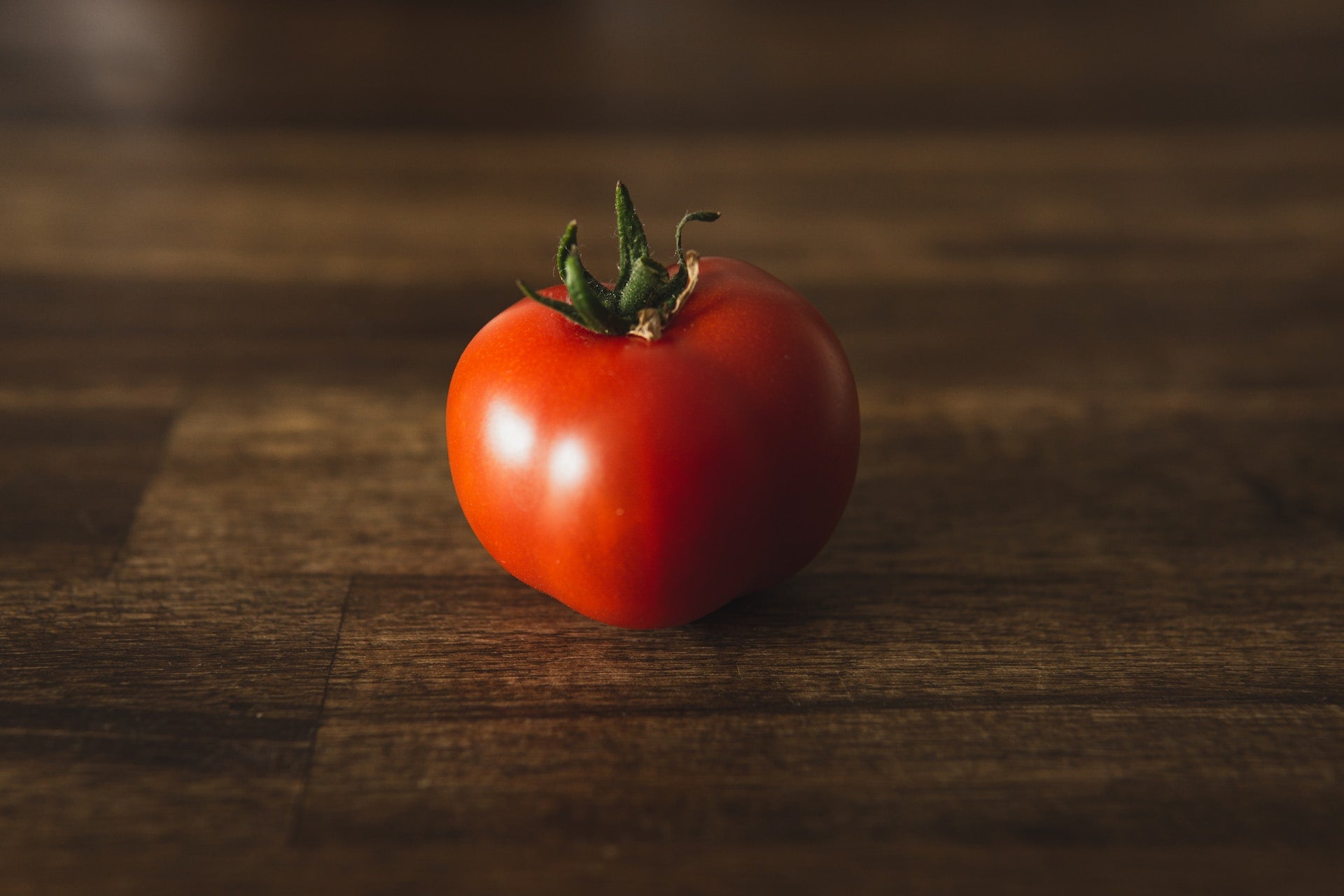 A single tomato, of the variety Slicing Caribe, stands in solitude, crowned with a beautiful green sepal, of which 7 protective green leaves protude. Resting on a stained wooden chopping block, the Slicing Caribe tomato stands in contemplation as to what awaits.