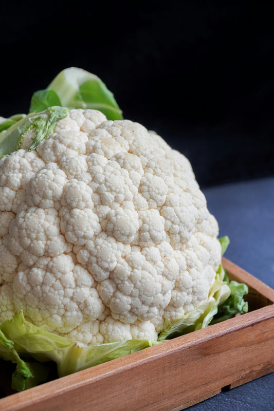 On display is a head of cauliflower, of the variety Snowball Y Improved.  It was previously harvested and is still wrapped in its green leaves. The cauliflower head has the typical brain appearance, except it is pure white.  Many white nodules on the head, small and large, all contribute to the fractal appeareance. 