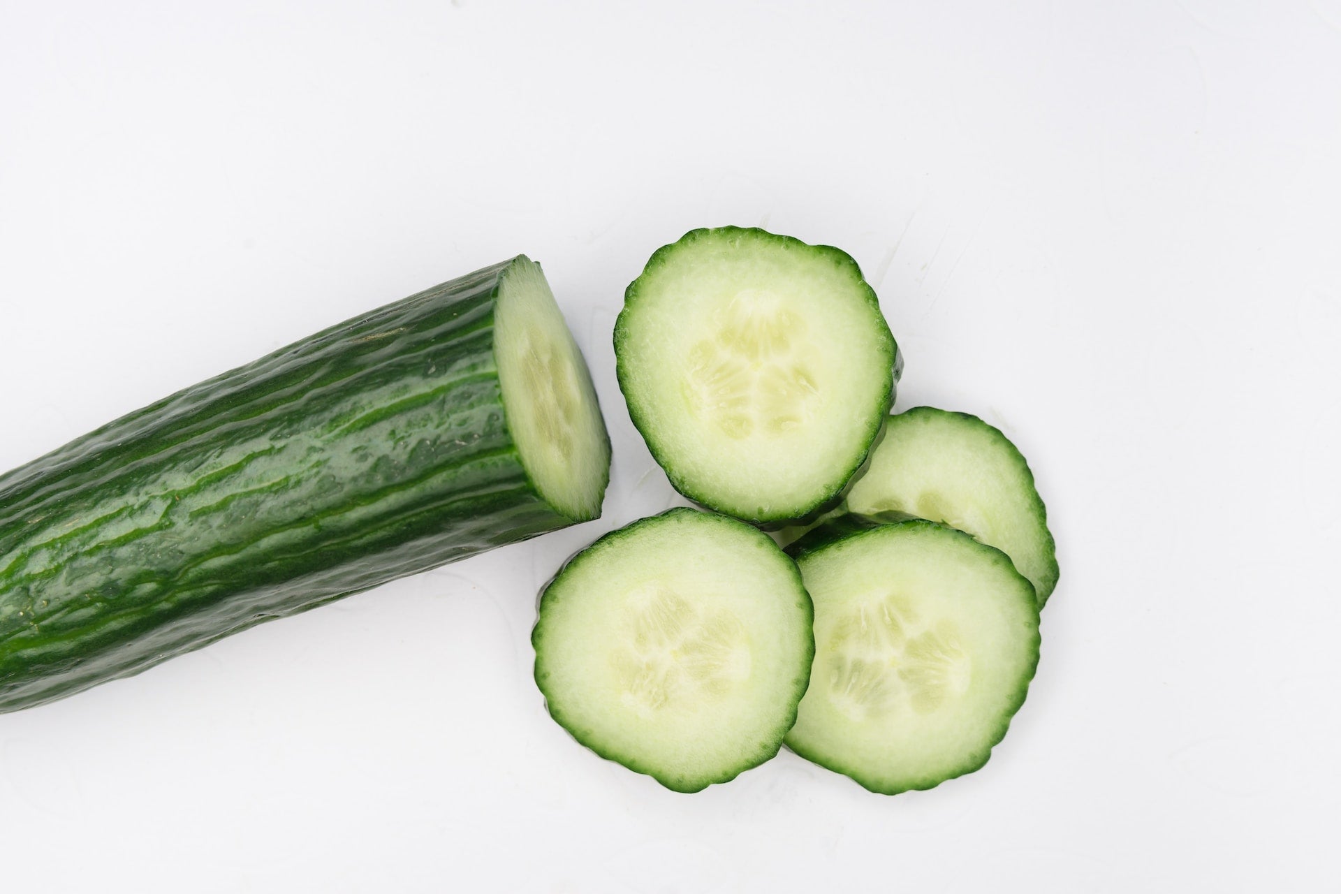On display is a single cucumber, of the variety Muncher. These particular cucumbers have the familiar smoothness one associates with typical cucumbers. The cucumber appears to have been sliced up to the midway point, with the slices stacked next to it. The cucumber and slices rest on a pure white surface.