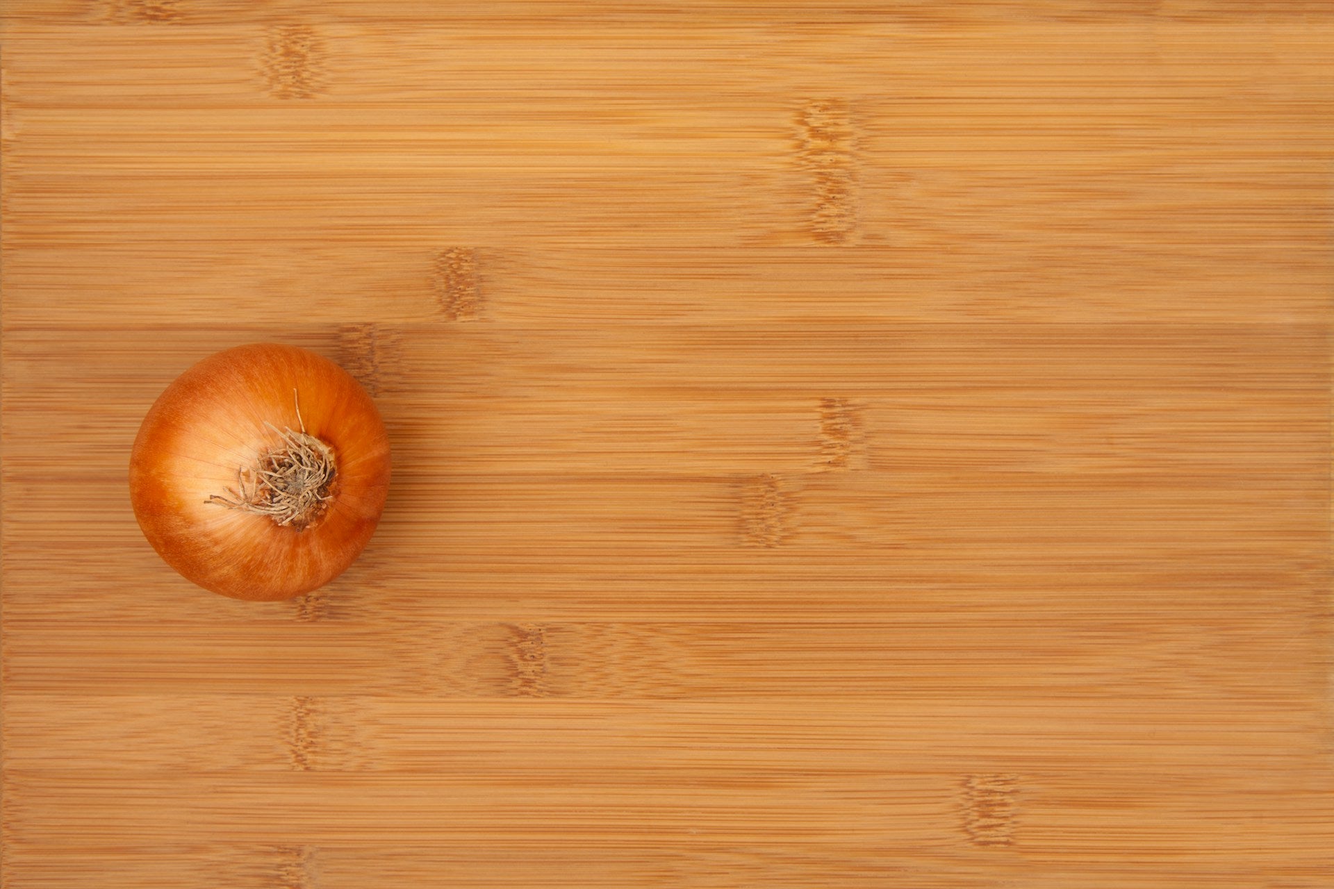 On display is a single yellow onion, of the variety Long Utah Yellow Sweet Spanish.  Freshly harvested, and fully washed, the onion is resting on a butcher block cutting board.
